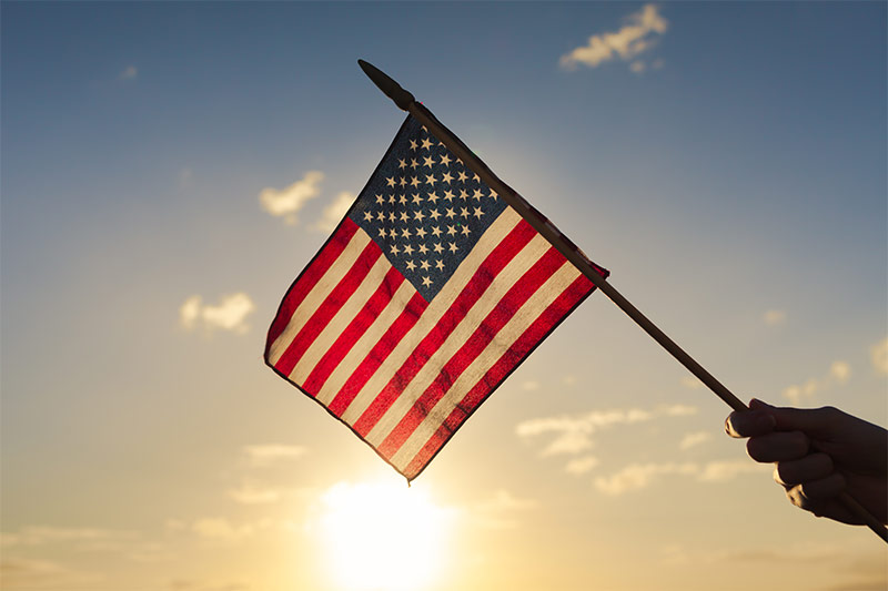 Hand holding United States flag against sunset