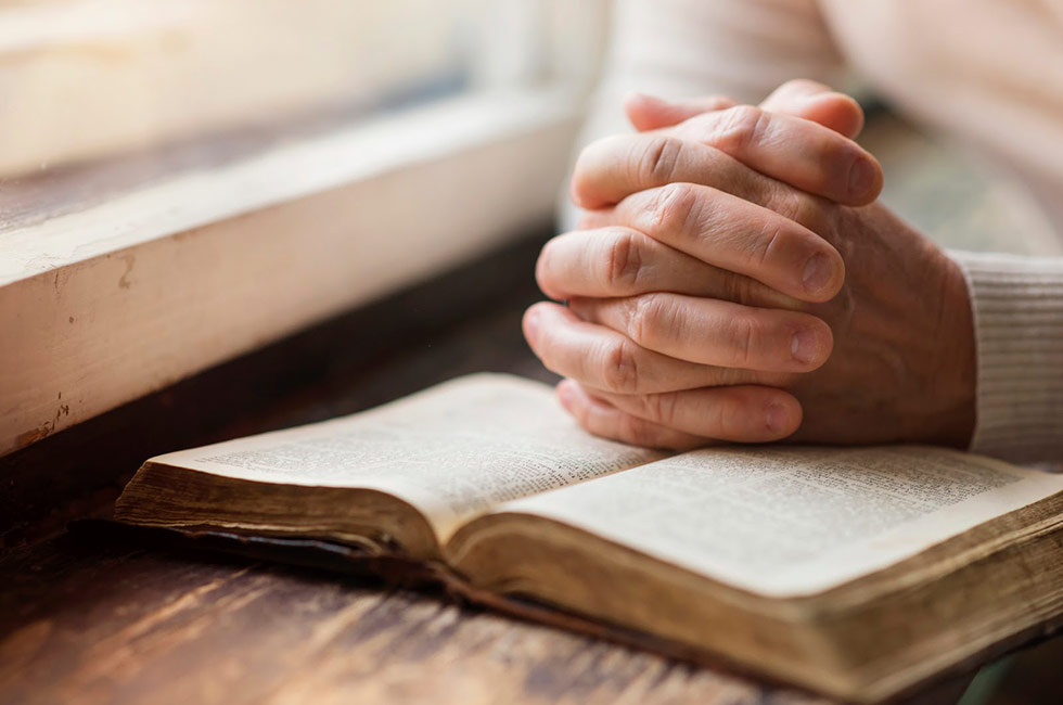 Hands folder over an open bible by a window