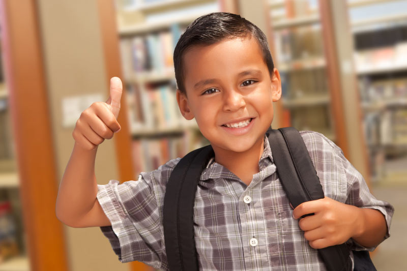 Photo of a little boy wearing a backpack and giving a thumbs up