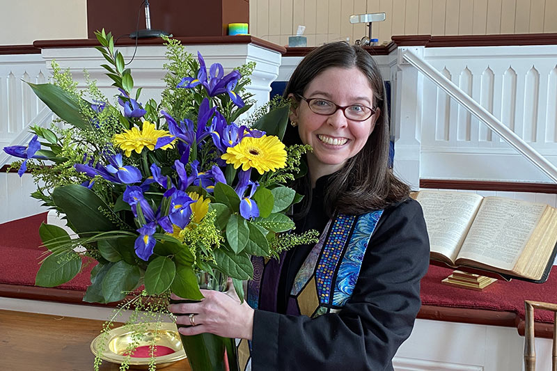 Photo of Reverend Rebecca Mygatt standing in the church holding flowers